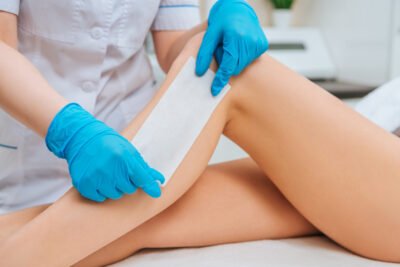 Partial view of cosmetologist in rubber gloves doing leg wax depilation