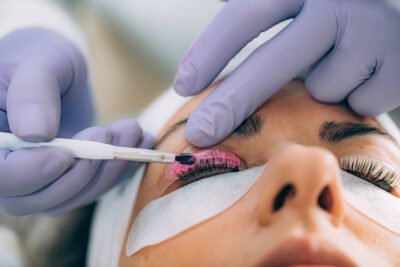 Cosmetologist Puts Pink Paint on the Eyelashes During Lash Lifting Procedure. Laminating Eyelashes.