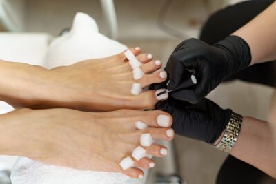 Specialist in beauty salon making french pedicure for female client. Relaxing at beauty salon, caring about nails.